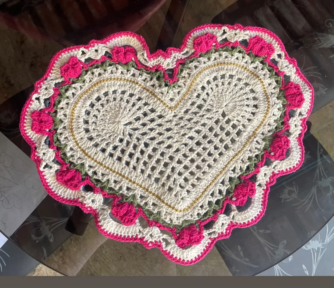 Peça em crochê no formato de coração, com detalhes rosa